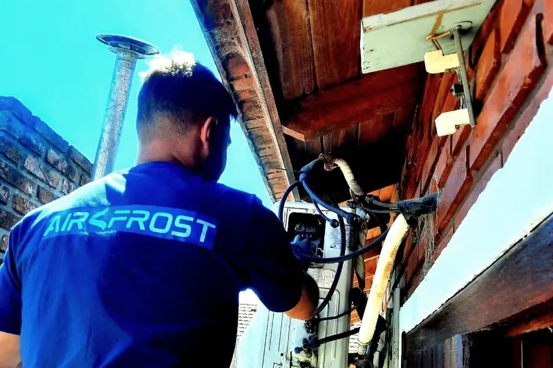 Técnico con remera de Air Frost trabajando sobre la unidad exterior de un equipo split en una vivienda
