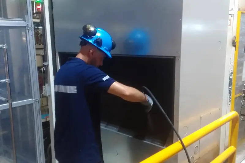 Técnico con casco y protección auditiva limpiando el serpentín de un equipo de climatización en una planta