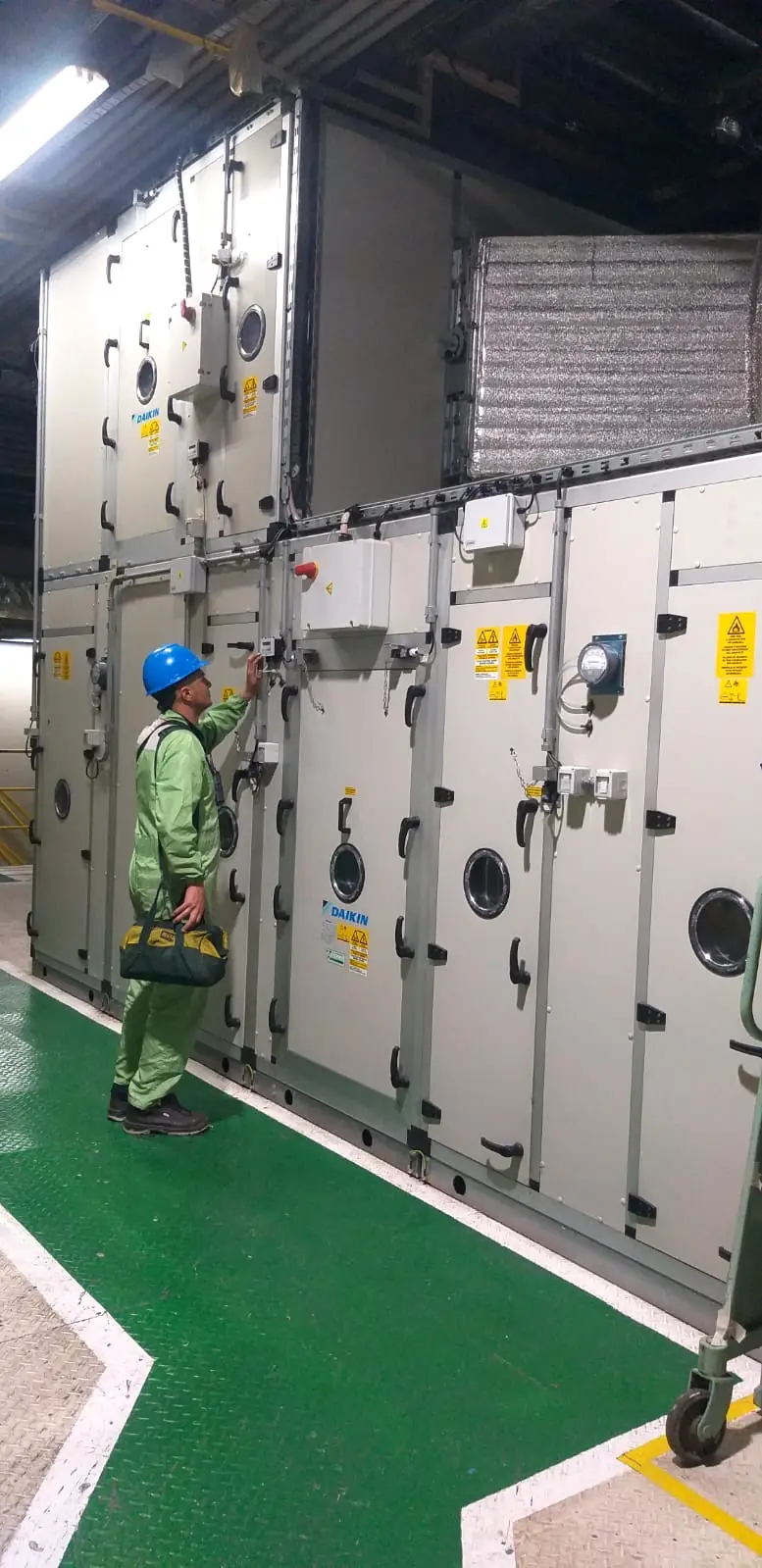 Técnico con casco revisando el tablero de una unidad de tratamiento de aire de gran porte en una planta industrial